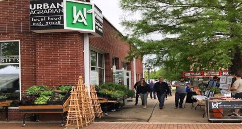 A street view of Urban Agrarian, featuring local food stands and shoppers outside a brick building.