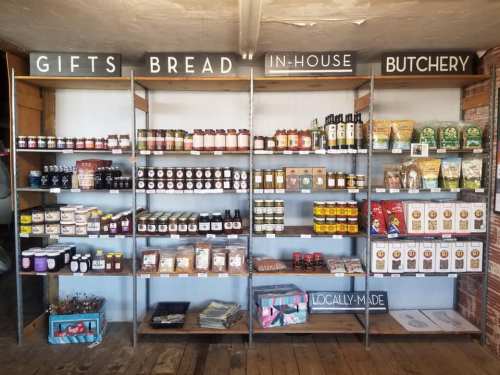 Shelves filled with jars, sauces, and packaged goods labeled "Gifts," "Bread," "In-House," and "Butchery."