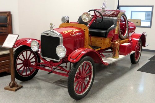 A vintage red fire truck with wooden accents, featuring a hose and ladder, displayed indoors.