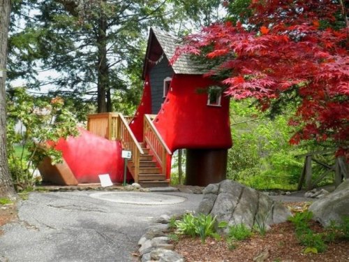 A whimsical red shoe-shaped house surrounded by trees and colorful foliage.