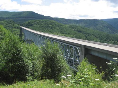 A long, elevated bridge stretches over lush green hills under a partly cloudy sky.