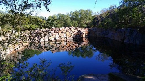 A serene quarry with a calm, reflective pond surrounded by trees and rocky formations.