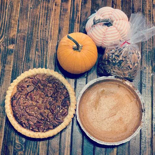 A pecan pie, a pumpkin pie, a bag of pecans, and two decorative pumpkins on a wooden table.