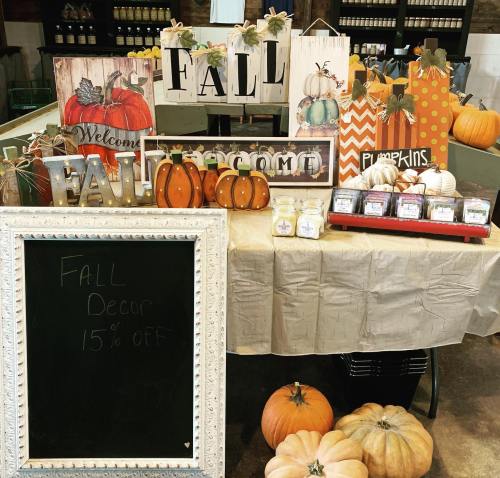 A display of fall decorations, including pumpkins, signs, and candles, with a chalkboard advertising 15% off.