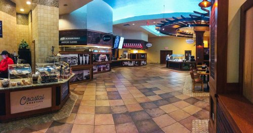 A spacious food court with various dining options, featuring a coffee shop and dessert displays, under bright lighting.
