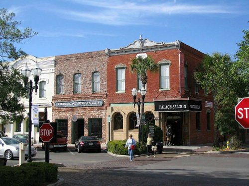 Historic brick buildings with shops, palm trees, and a clear blue sky in a charming town square.