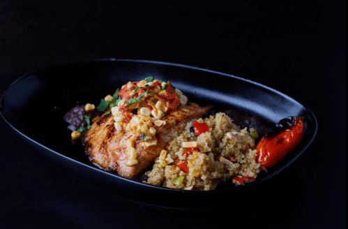 Grilled salmon topped with corn salsa, served with quinoa and roasted red pepper on a black plate.