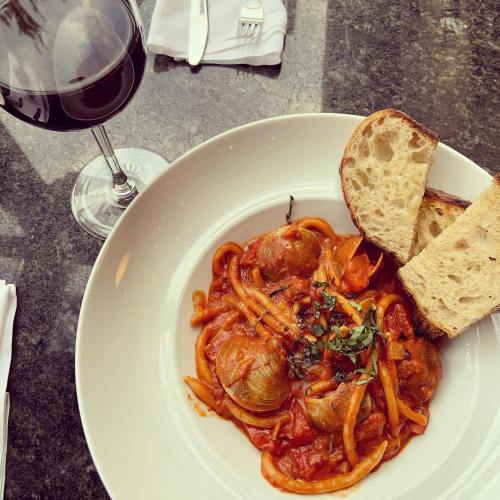 A bowl of pasta with meatballs in tomato sauce, garnished with herbs, served with two slices of bread and a glass of red wine.