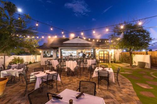 Outdoor dining area with tables set for guests, string lights overhead, and a cozy restaurant in the background at dusk.