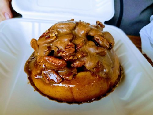 A dessert featuring a round base topped with a thick layer of pecans and a glossy caramel sauce.