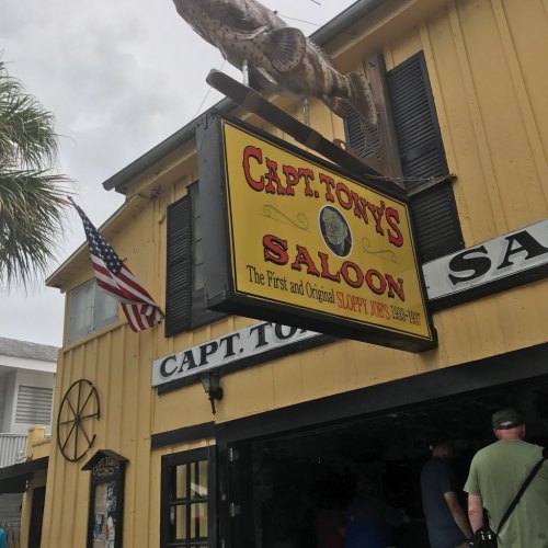 Sign for Capt. Tony's Saloon, a historic bar in Key West, with an American flag and patrons visible outside.