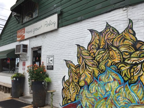 Colorful mural of abstract leaves on a white brick wall beside a building with a sign for parking.