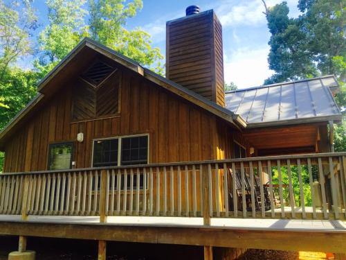 A wooden cabin with a chimney, surrounded by trees, featuring a front deck and large windows.