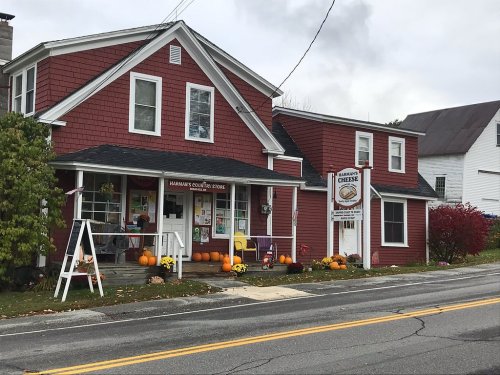 A red two-story building with pumpkins on the porch, featuring a sign for a local store and a cheese shop.