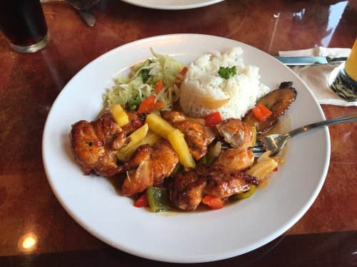 A plate of grilled chicken with pineapple, mixed vegetables, rice, and a side of cabbage salad.