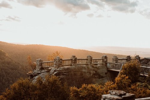 Scenic view from a rocky overlook at sunset, with stone railings and lush green mountains in the background.