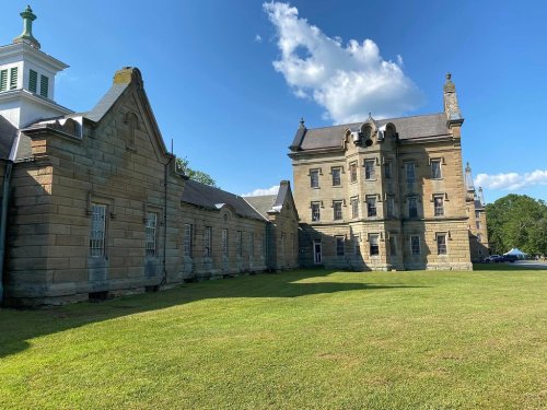 Historic stone building with a grassy area, under a blue sky with clouds.