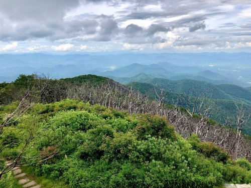 A panoramic view of lush green mountains under a cloudy sky, with layers of hills fading into the distance.