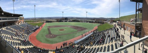 A panoramic view of a baseball field with empty stands and a clear blue sky in the background.