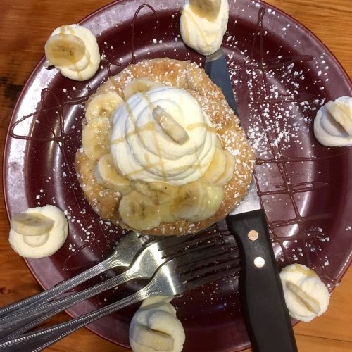A dessert with a fluffy base topped with whipped cream, banana slices, and drizzled with syrup, surrounded by mini whipped cream dollops.