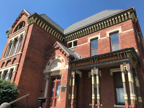 Historic red brick house with ornate architectural details and colorful columns under a clear blue sky.