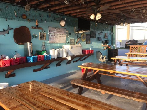 Outdoor dining area with wooden tables, colorful baskets, and a blue wall decorated with fishing-themed decor.