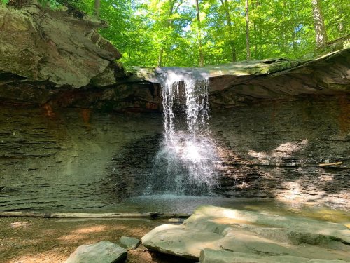 A serene waterfall cascading over rocky cliffs, surrounded by lush green trees in a peaceful forest setting.