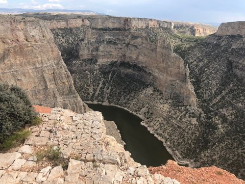 Aerial view of a deep canyon with a winding river at the bottom, surrounded by rocky cliffs and sparse vegetation.