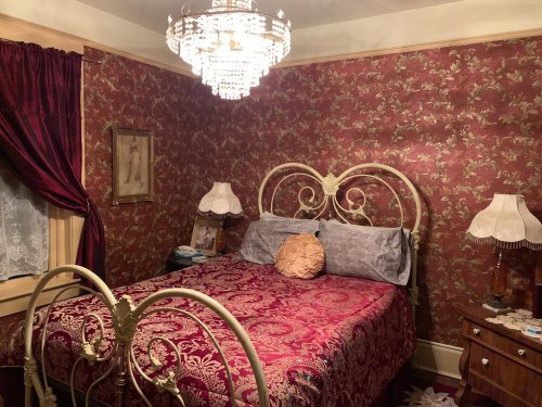 Cozy bedroom with a vintage bed, ornate chandelier, floral wallpaper, and elegant lamps on bedside tables.