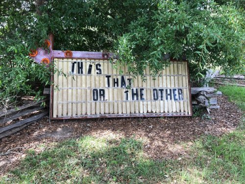 A weathered sign partially obscured by greenery reads, "THIS OR THAT OR THE OTHER."