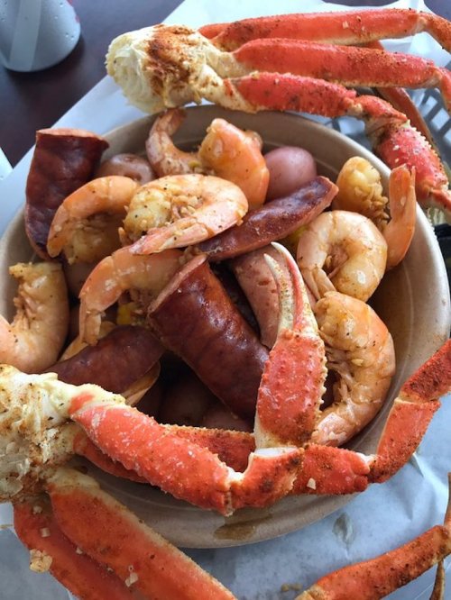 A bowl filled with shrimp, crab legs, sausage, and potatoes, seasoned and ready to eat.