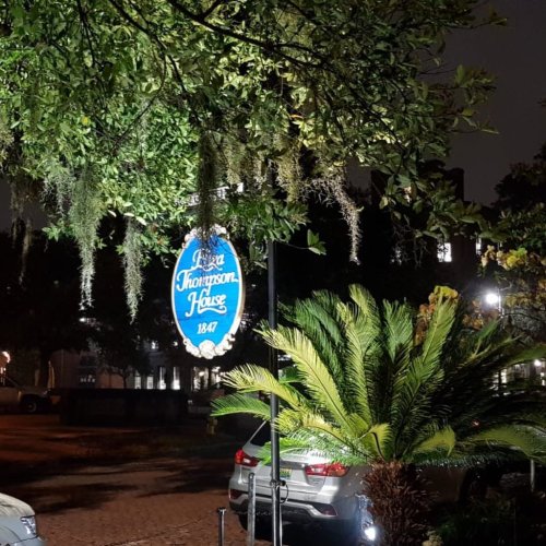 A night view of a sign reading "Thompson House 1847," surrounded by greenery and illuminated by soft lighting.
