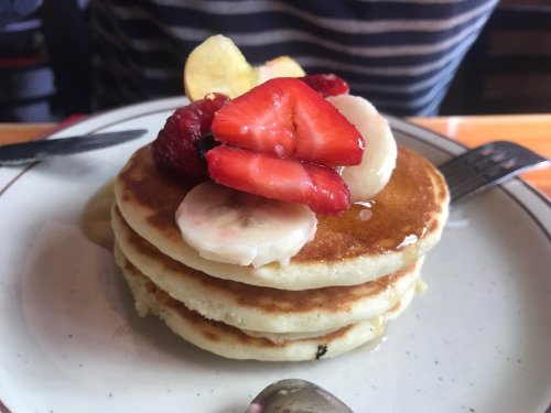 A stack of fluffy pancakes topped with sliced strawberries, bananas, raspberries, and a drizzle of syrup.
