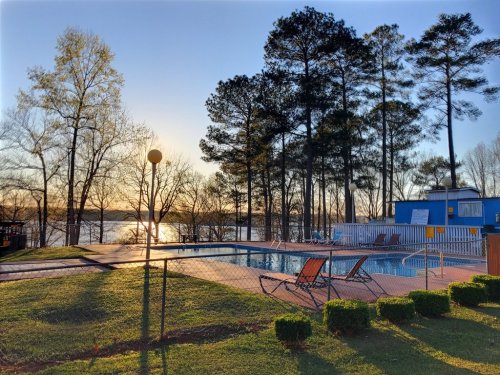 A serene poolside view at sunset, surrounded by trees and overlooking a calm lake.