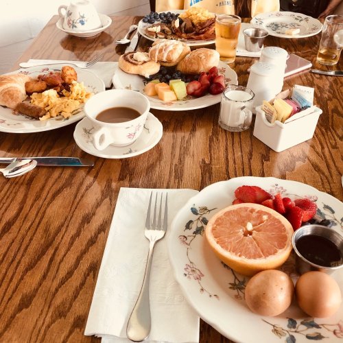 A table set with plates of breakfast food, including eggs, fruit, pastries, and coffee, in a cozy dining setting.