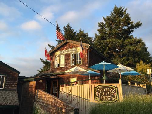 A rustic restaurant with a wooden exterior, flags, and outdoor seating under umbrellas, surrounded by trees.