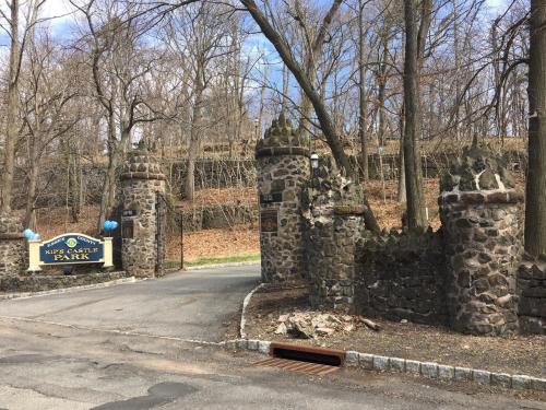 Entrance to Kips Castle Park featuring stone gates and a sign, surrounded by bare trees and a hilly landscape.