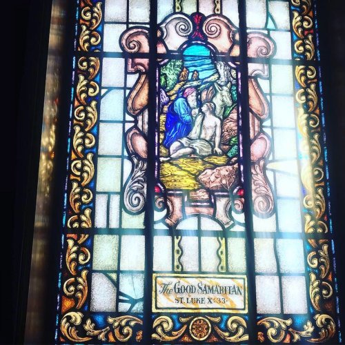 Stained glass window depicting the Good Samaritan, featuring vibrant colors and intricate designs.