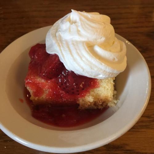 A slice of cake topped with strawberries and whipped cream, served on a small white plate.