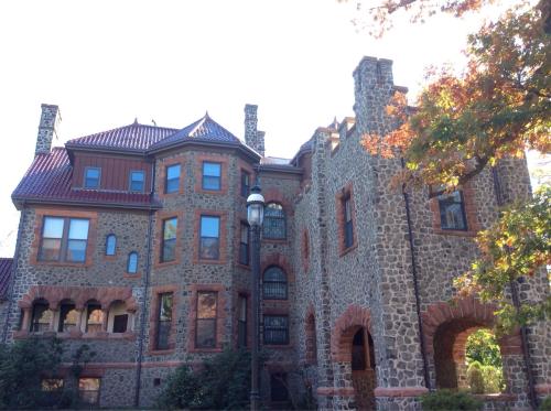 A large stone mansion with a mix of architectural styles, featuring a red-tiled roof and decorative stonework.