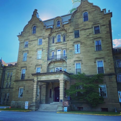 Historic stone building with ornate architecture, featuring a central entrance and large windows under a clear blue sky.