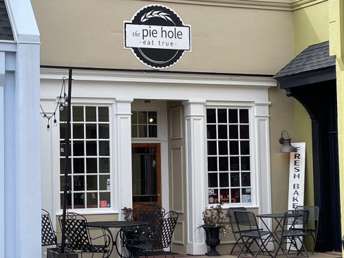 Exterior of "The Pie Hole" bakery, featuring a sign and outdoor seating with tables and chairs.