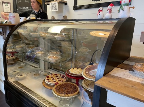 A display case filled with various pies and desserts, with a barista in the background and festive decorations.