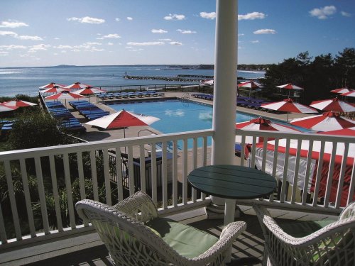 A scenic view of a pool area with lounge chairs and umbrellas, overlooking the ocean under a clear blue sky.