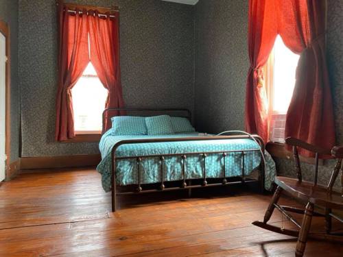 Cozy bedroom with a metal bed, patterned walls, red curtains, and a wooden rocking chair.