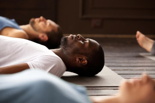 A group of people lying on yoga mats in a serene setting, practicing relaxation or meditation.