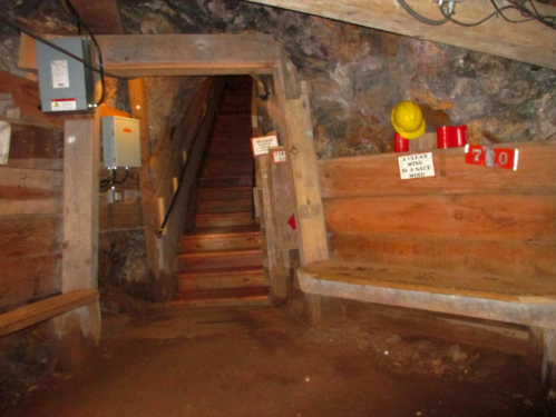 Interior of a mine with wooden beams, stairs leading up, benches, and safety equipment on the walls.