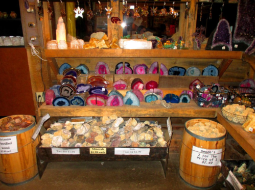 A wooden display shelf filled with various colorful crystals and geodes, with price tags visible.