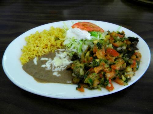 A plate of colorful Mexican food featuring yellow rice, refried beans, salad, and a vegetable medley.