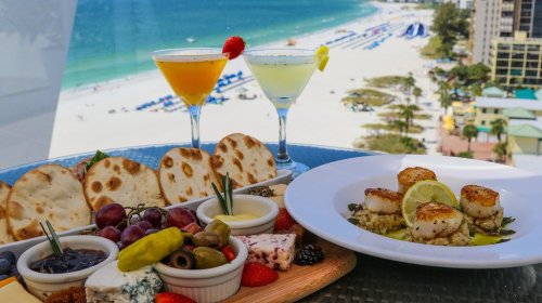 A vibrant beachside meal featuring cocktails, a gourmet platter, and seared scallops with a scenic ocean view.